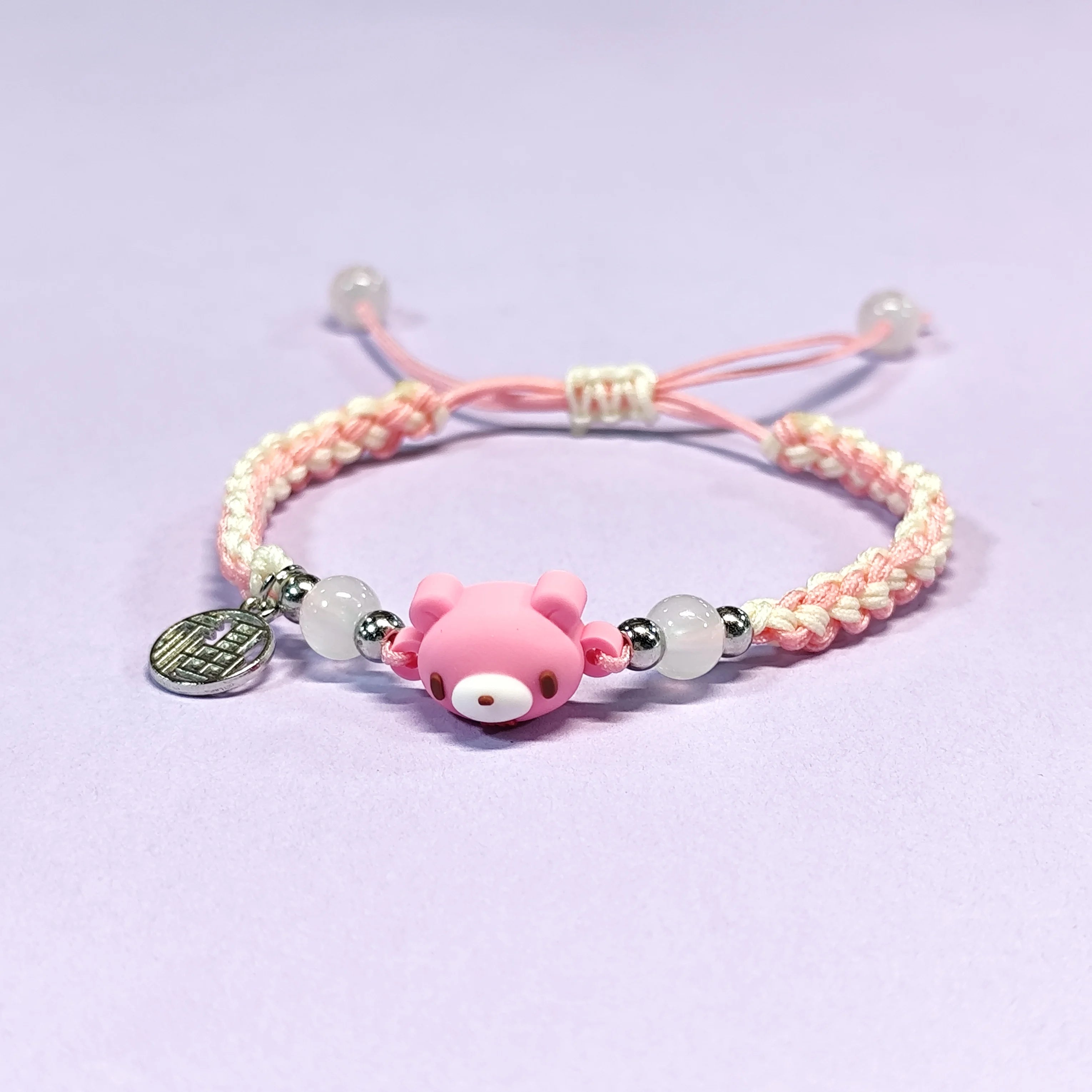 Hand - braided bracelet with a pink bear charm, beads, and a silver pendant. Cute and delicate accessory.